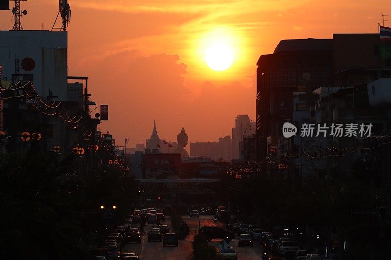 橙色的夕阳天空在佛祖Dhammakaya Thep Mongkol(青铜雕像)和Wat Paknam Bhasicharoen(皇家寺庙)之上，从立交桥上看高速公路上的交通堵塞，摩托车，汽车，空气污染，烟雾，汽车烟雾，重点在前景